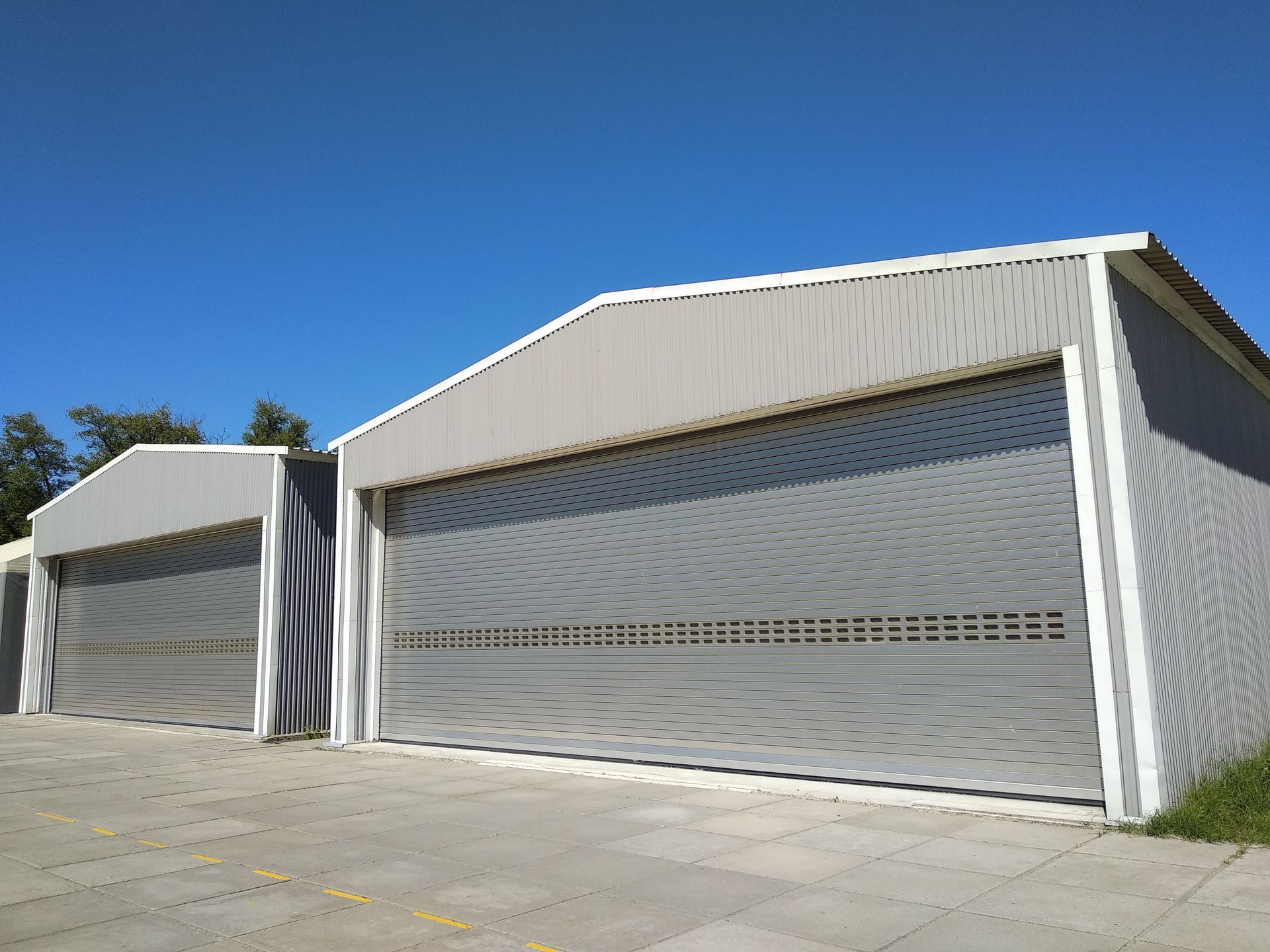 Two grey metal storage units or hangars with roll-up doors against a clear blue sky.