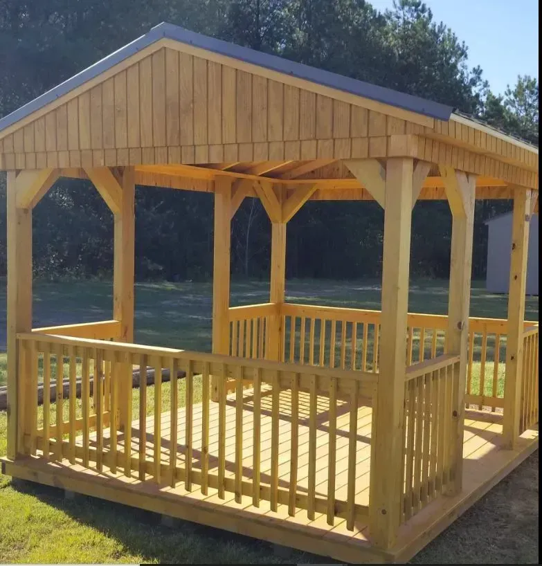 A wooden gazebo with a gabled roof and railings, standing on a grass lawn.