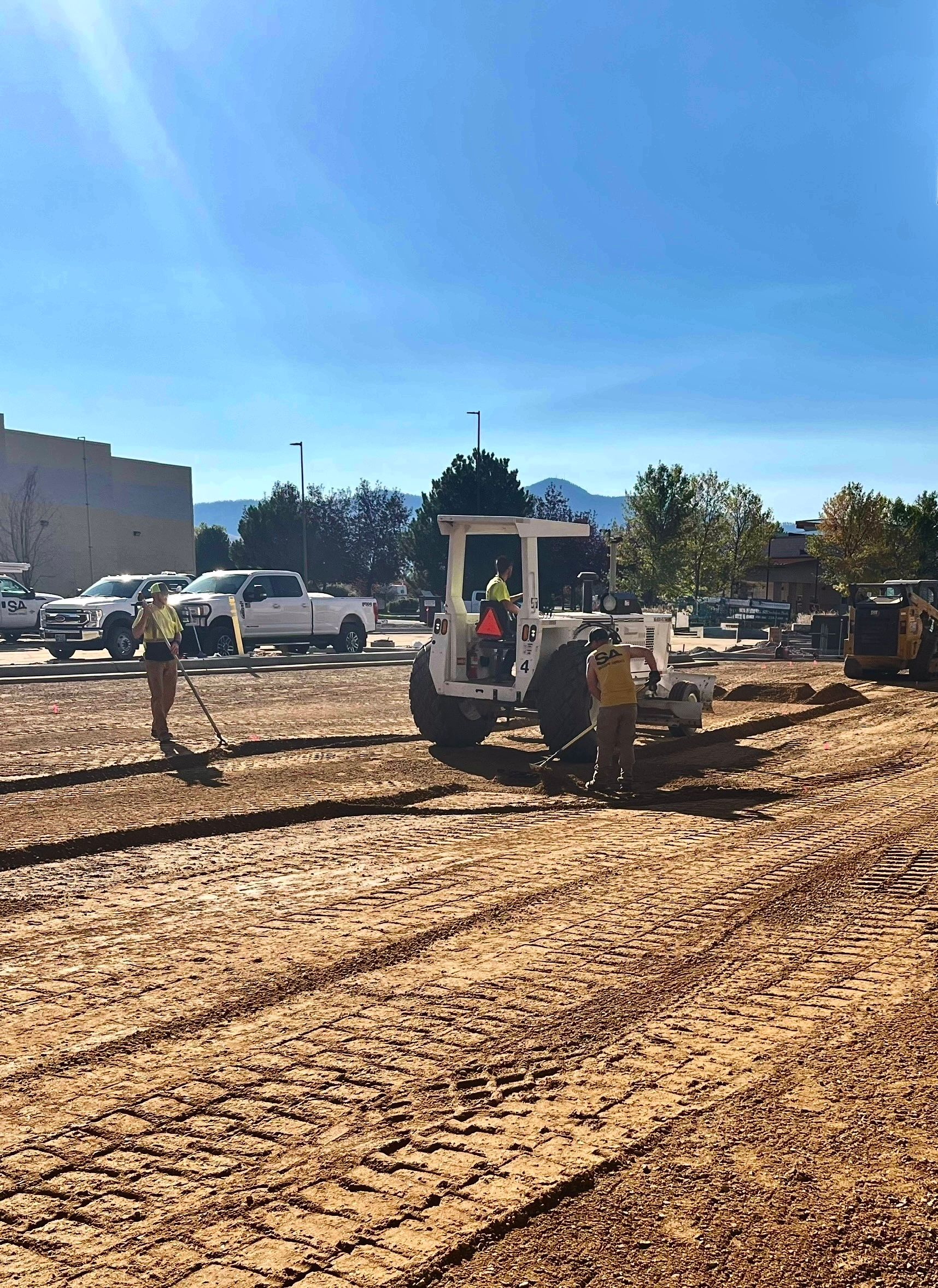 Construction site with a white tractor grading dirt under a clear blue sky.