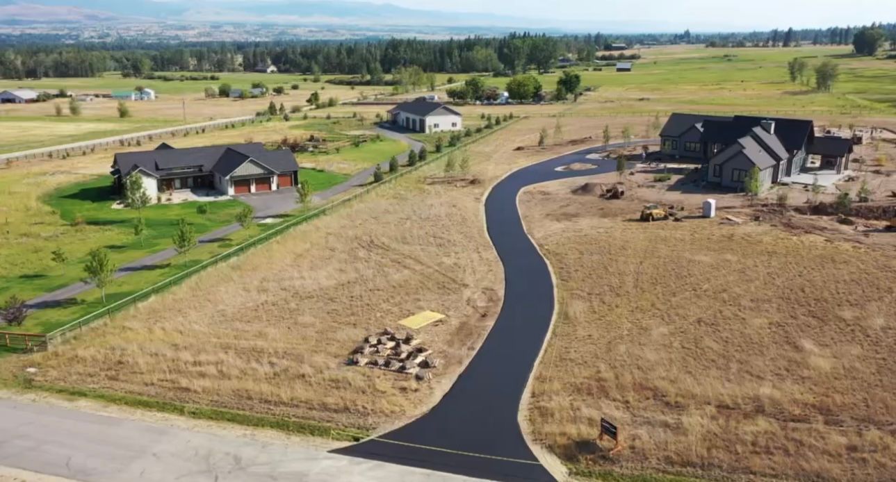 Aerial view of newly paved road leading to houses in a grassy field.