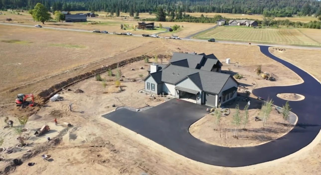 Aerial view of a new house with dark asphalt driveway under construction, surrounded by a field.