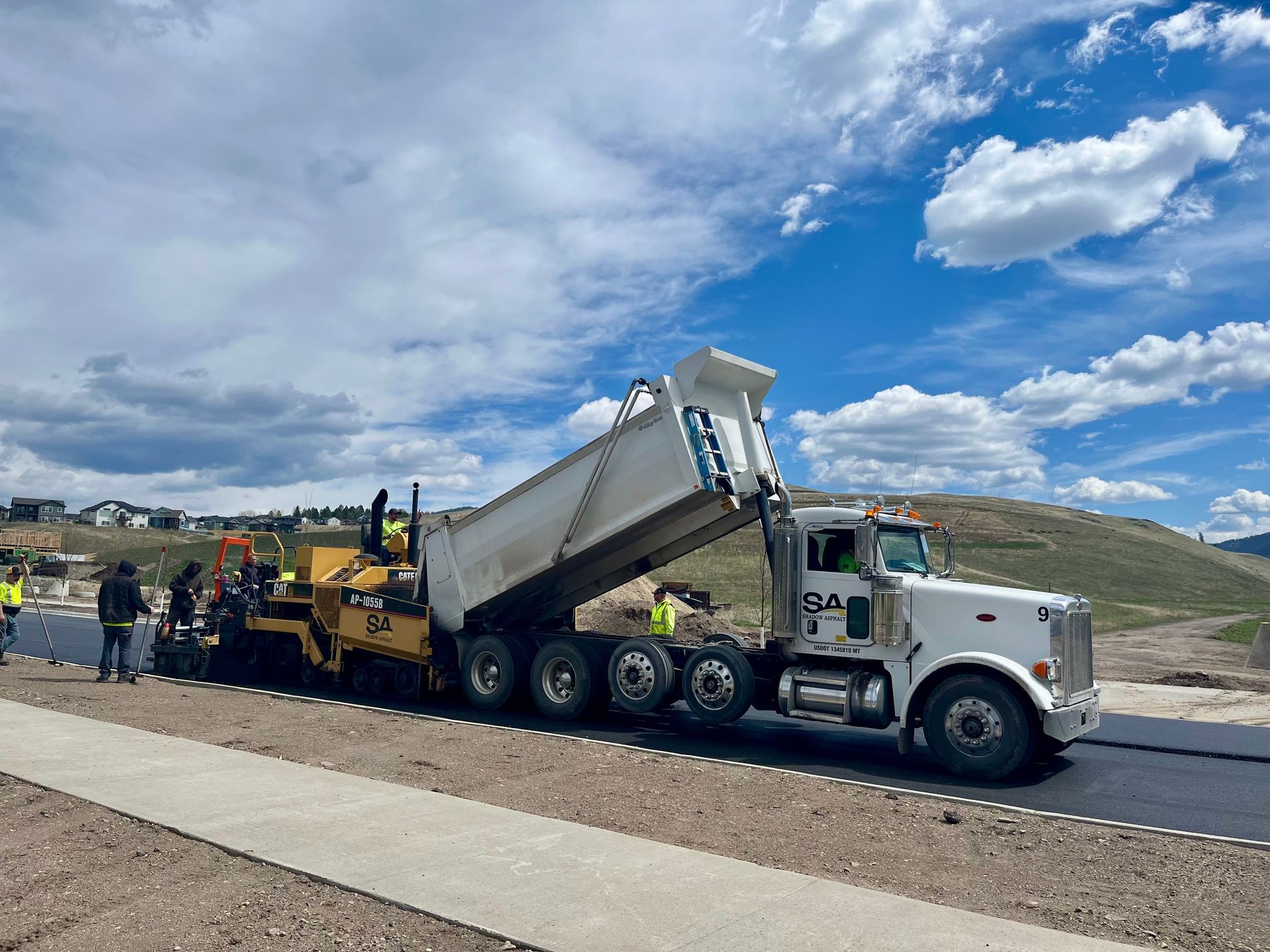 White dump truck unloading asphalt into a paving machine on a road construction site. Blue sky.