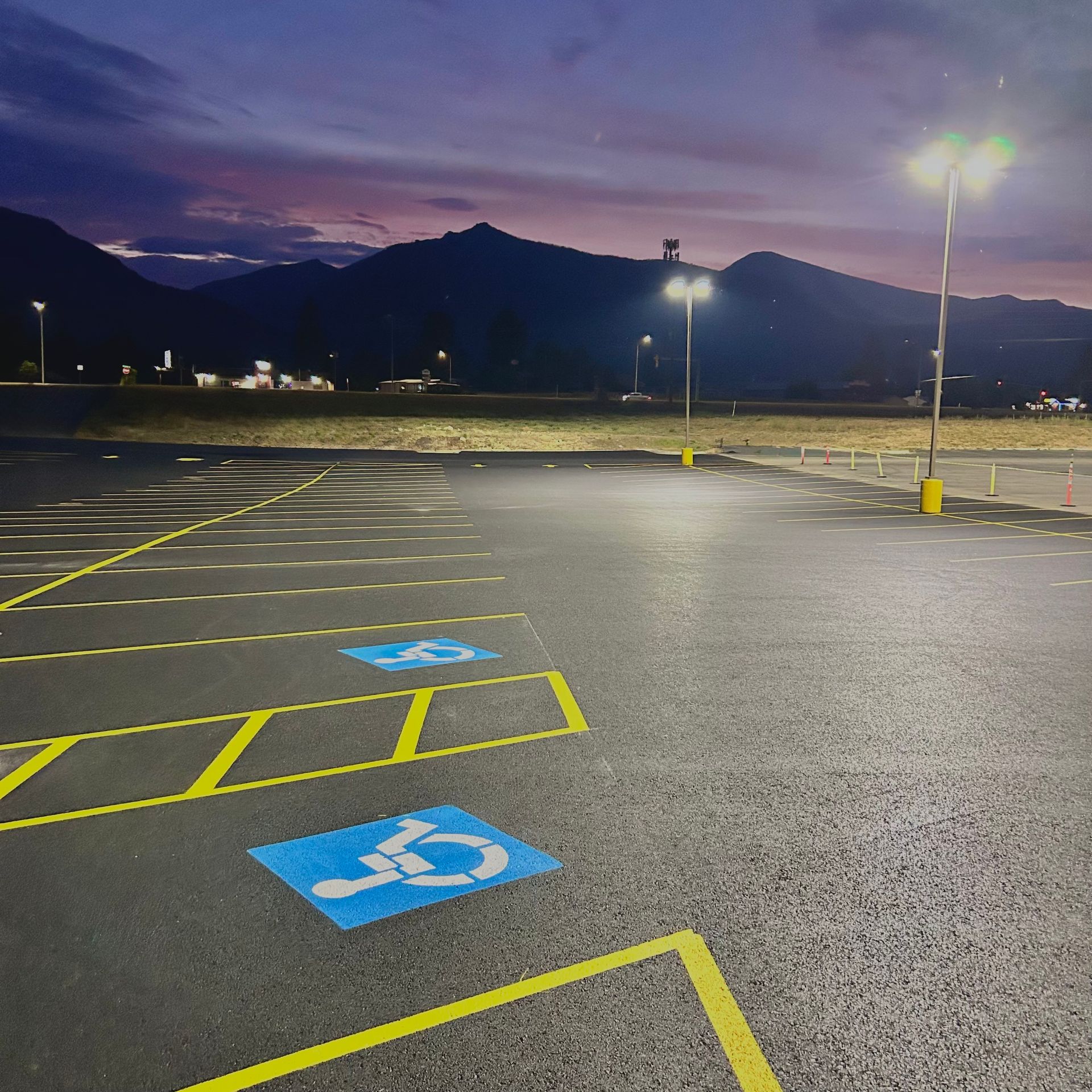 Empty asphalt parking lot at dusk, with mountain backdrop and handicapped parking spaces marked with blue symbols and yellow lines.