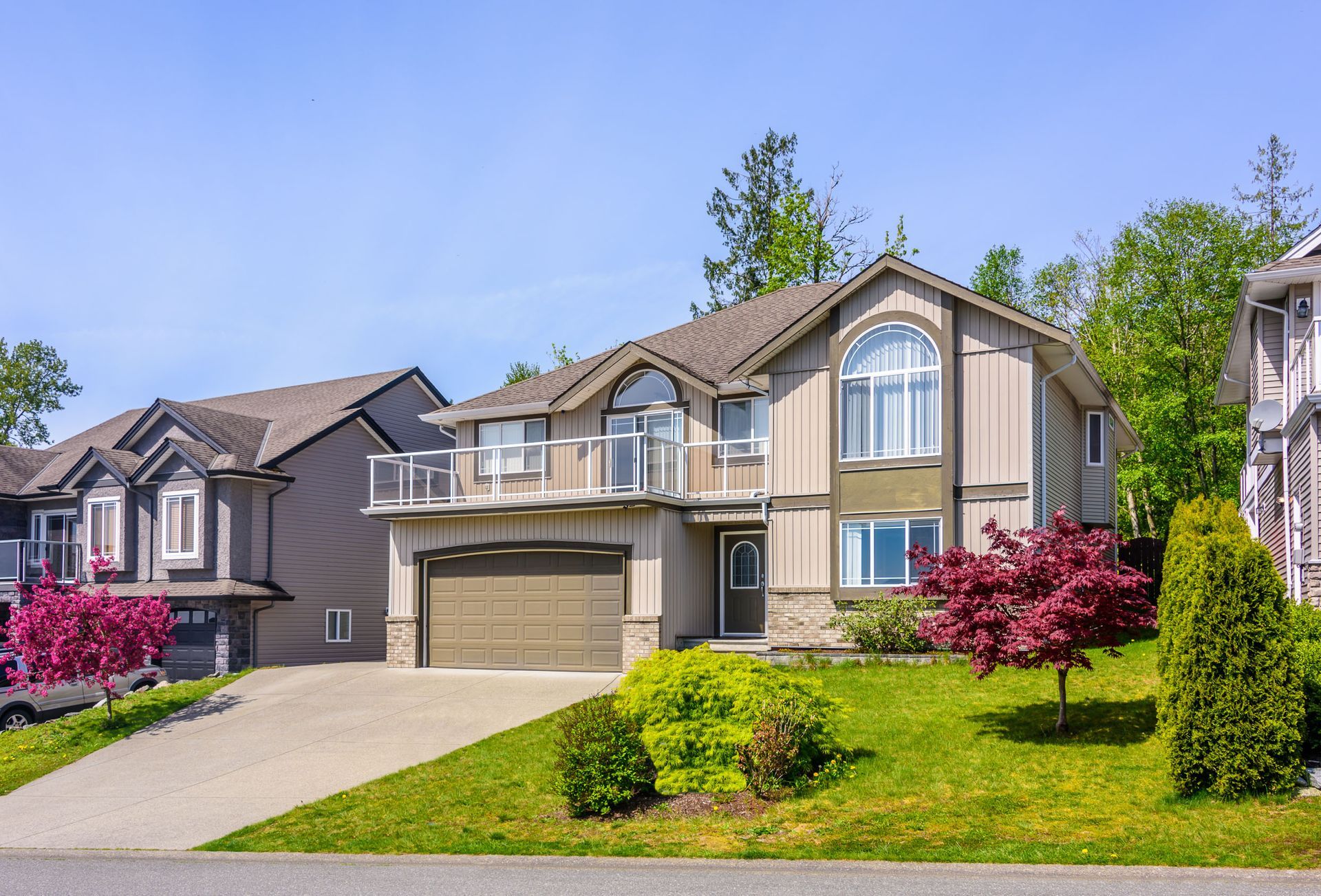 A large house with a large garage is sitting on top of a lush green hillside.