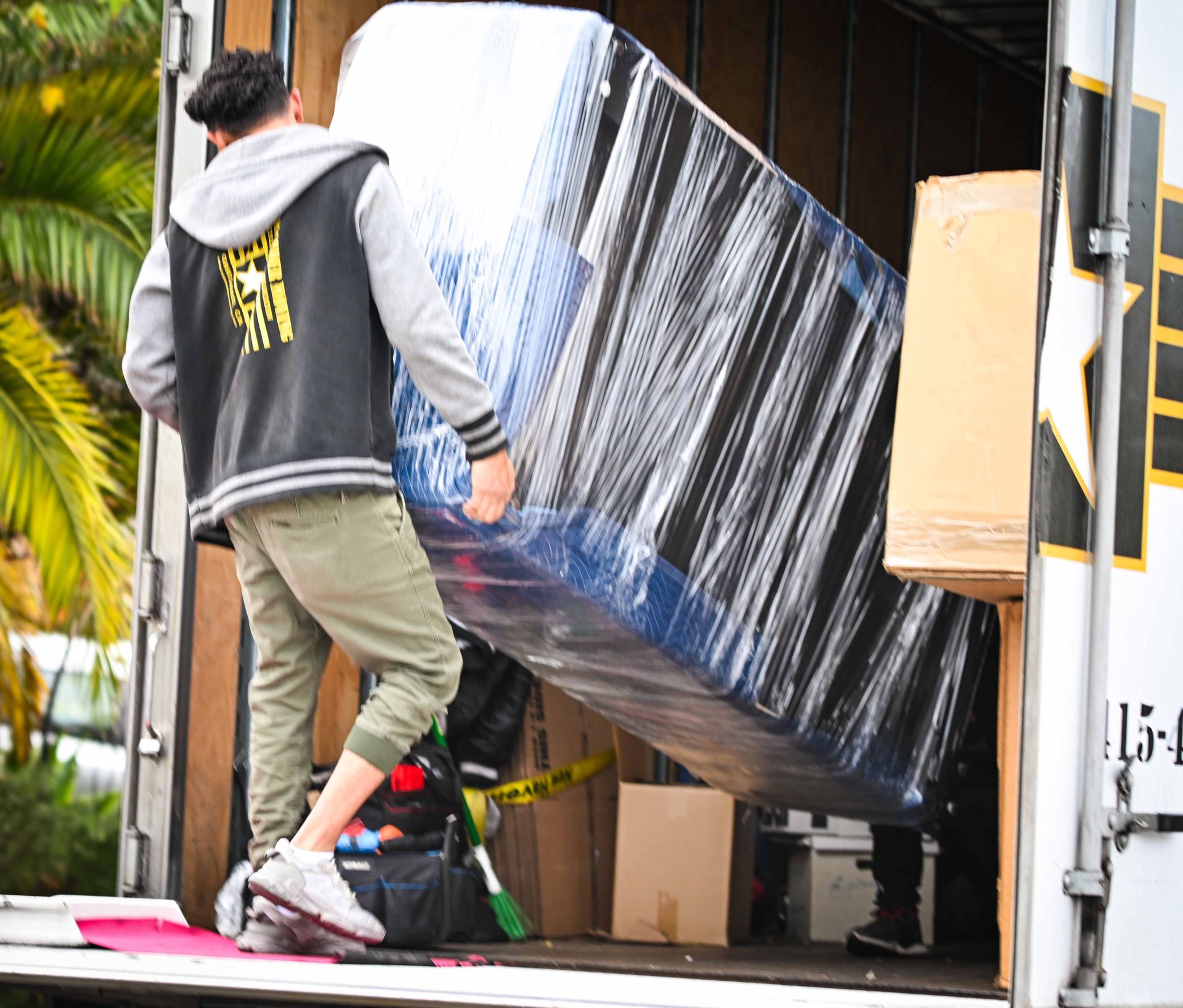 A person carrying a wrapped, blue and white furniture item into a moving truck.