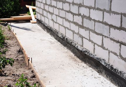 Gray house siding with a dark vertical pole in the foreground, showing visible space between the house and the dirt ground.
