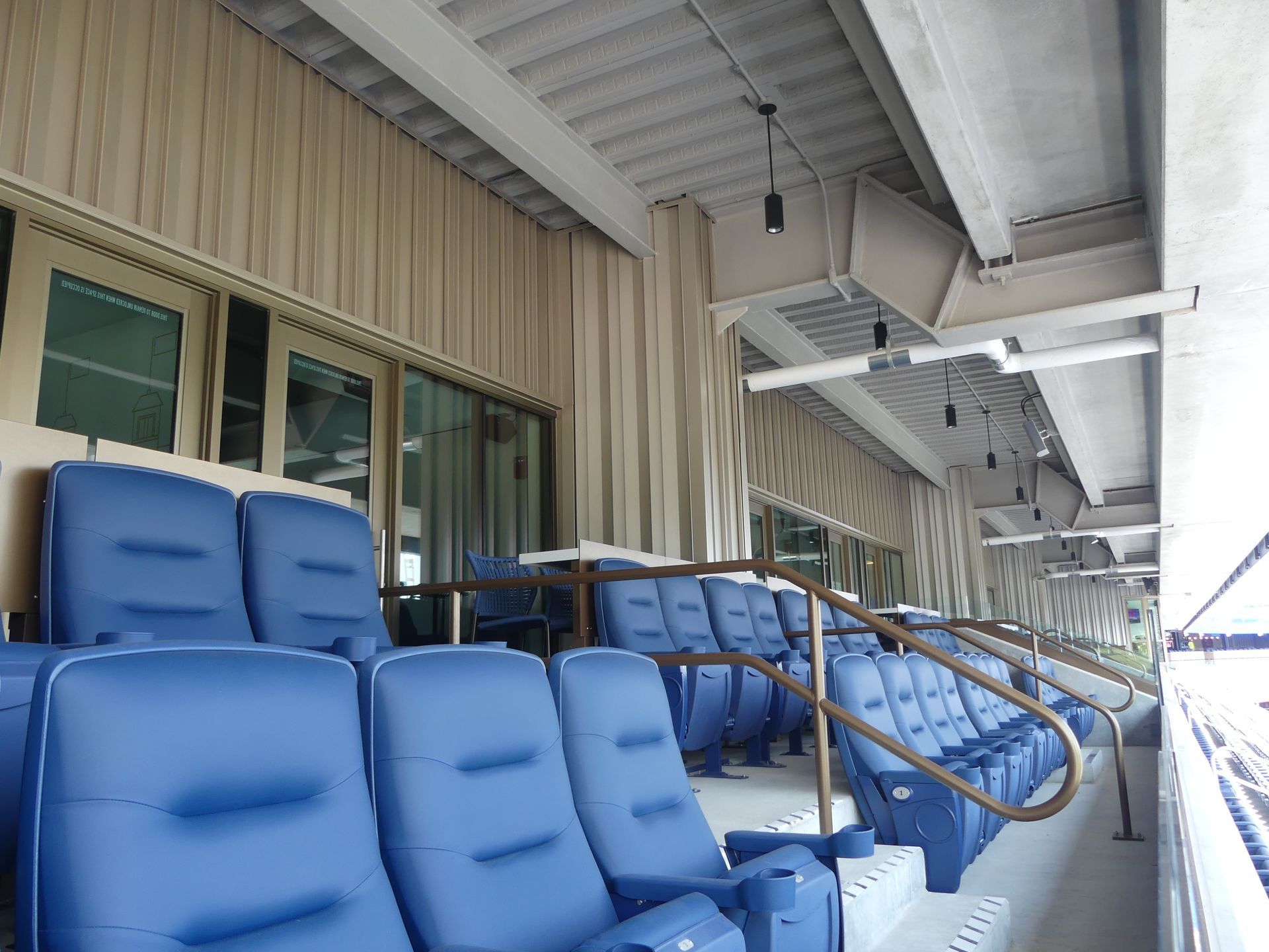 Blue stadium seating under a covered area with curtains.