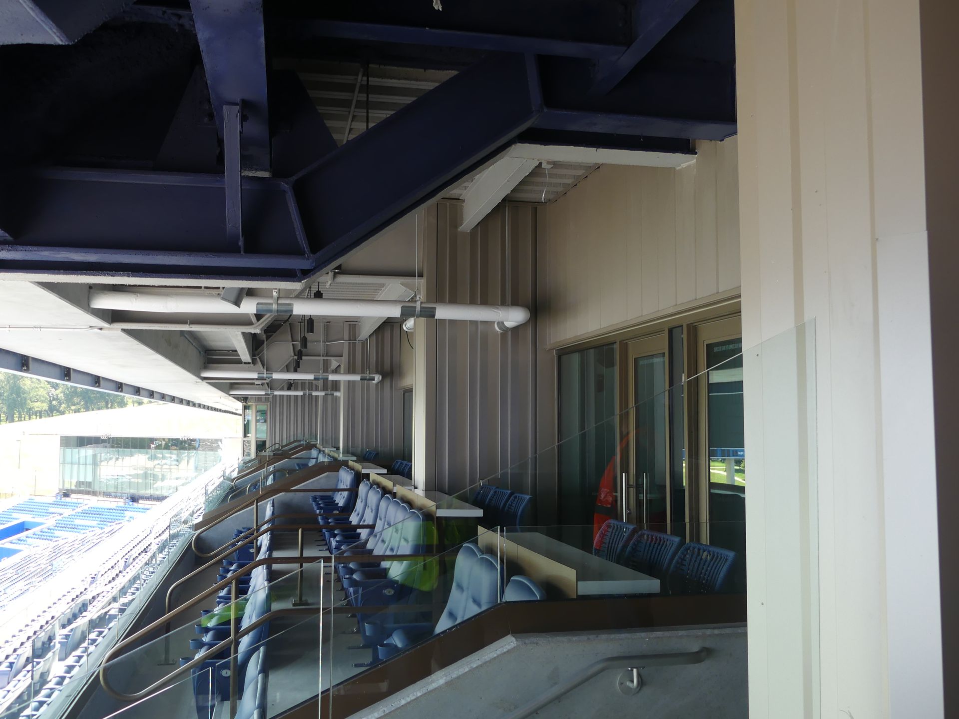 Bleachers with blue chairs, under a dark metal beam structure.