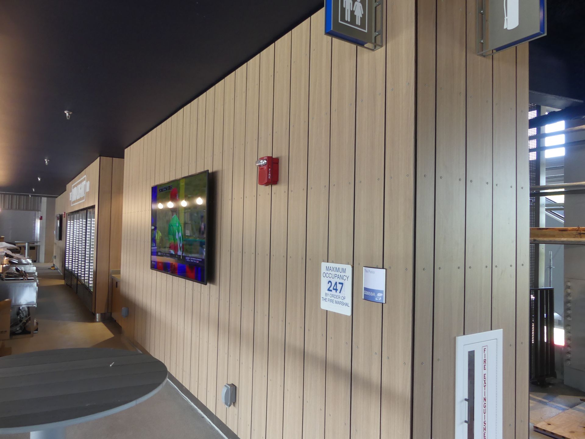 Interior wall with wood paneling, TV, and restroom signs; modern design.