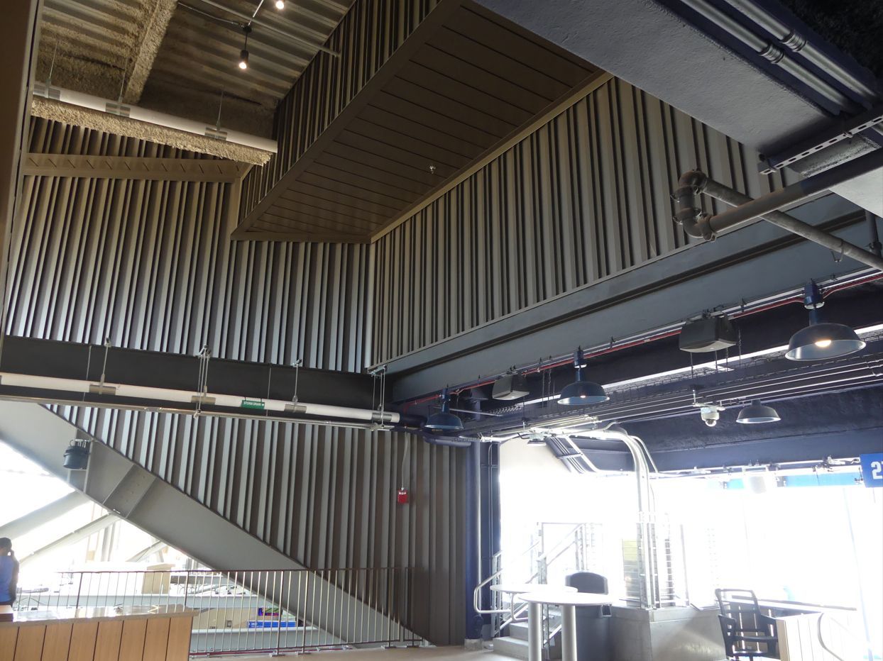 Interior of a modern building under construction, showing metal beams, corrugated walls, and a staircase.
