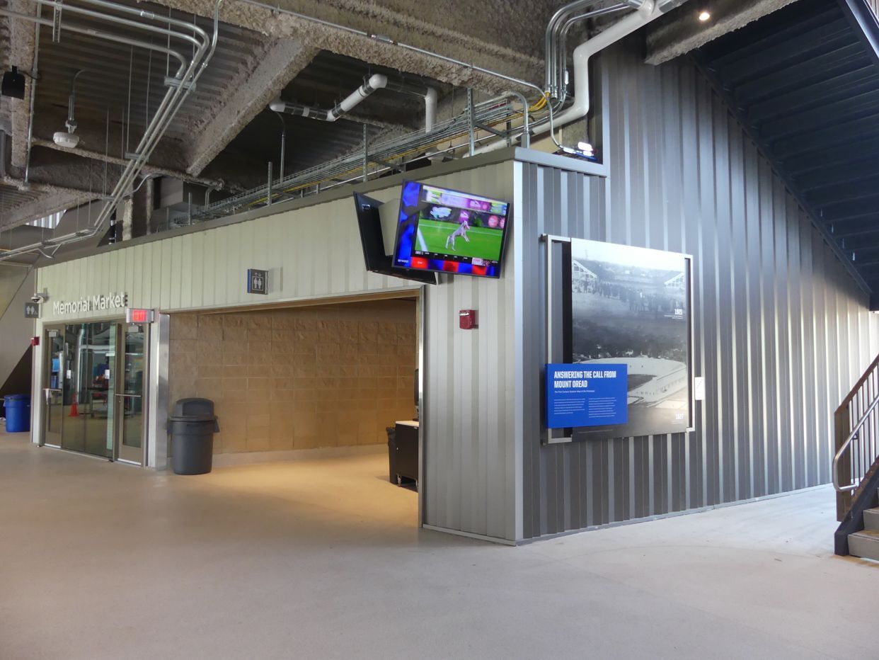Indoor area with a TV showing a sports game, a doorway, and corrugated metal walls.