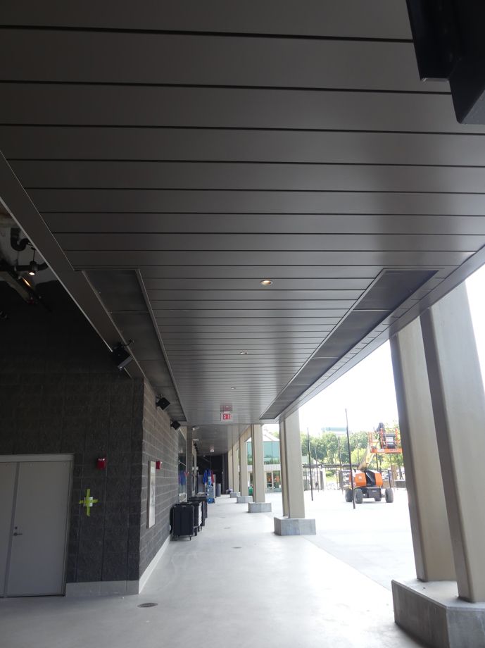 A long, covered outdoor walkway with gray ceiling panels and white pillars.