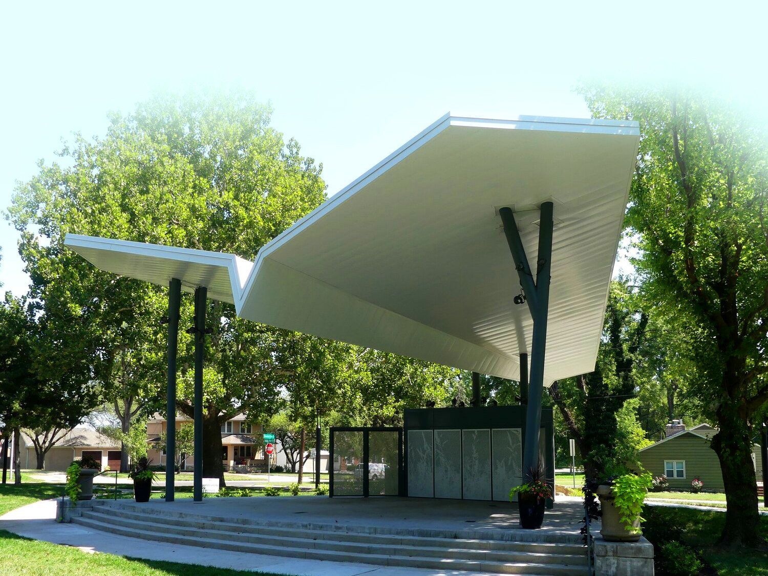 A stage with a wing-like roof in a park with trees in the background