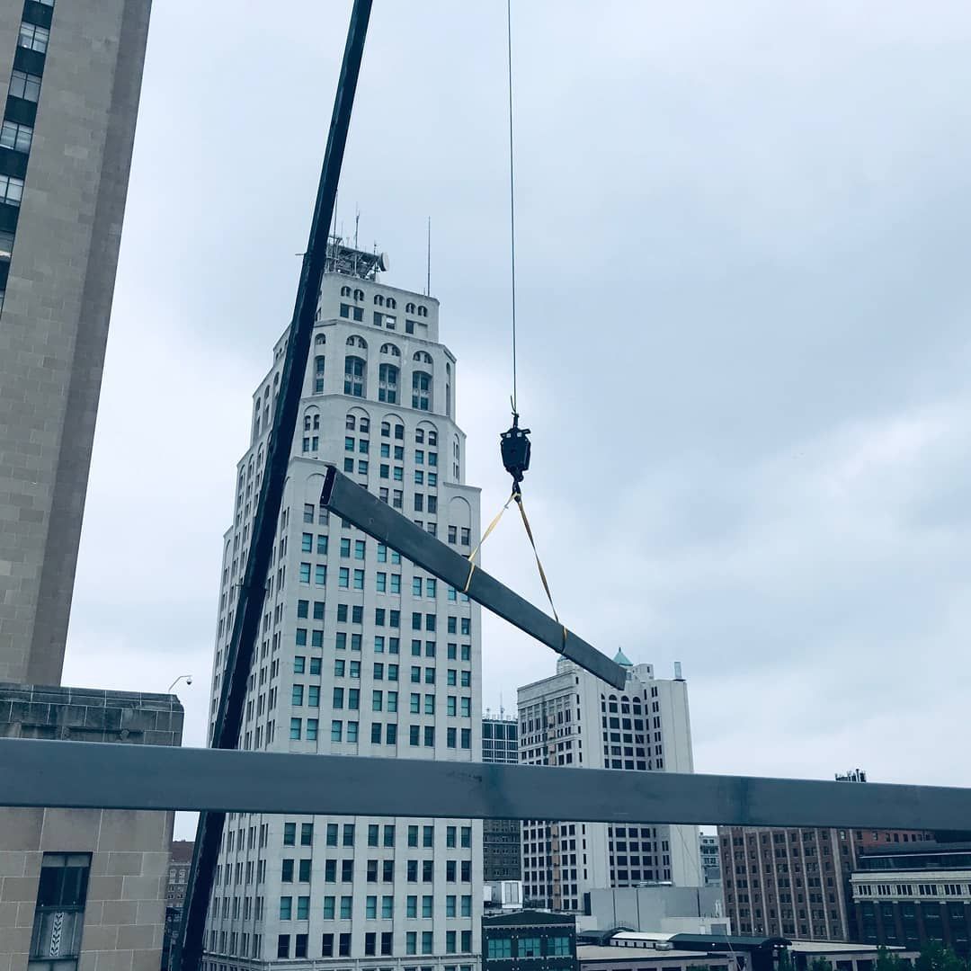 A crane is lifting a piece of metal in front of a tall building