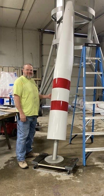 A man in a yellow shirt is standing next to a large red and white pole.