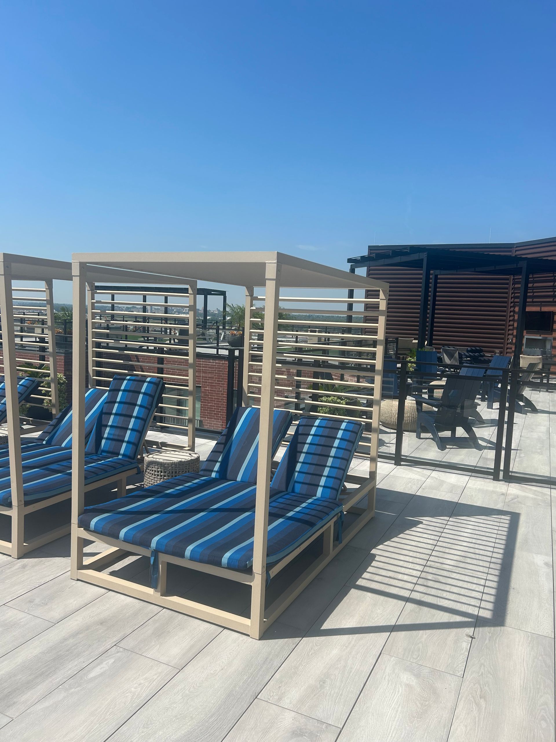 Lounge chairs with blue striped cushions under a pergola on a rooftop patio; sunny day.