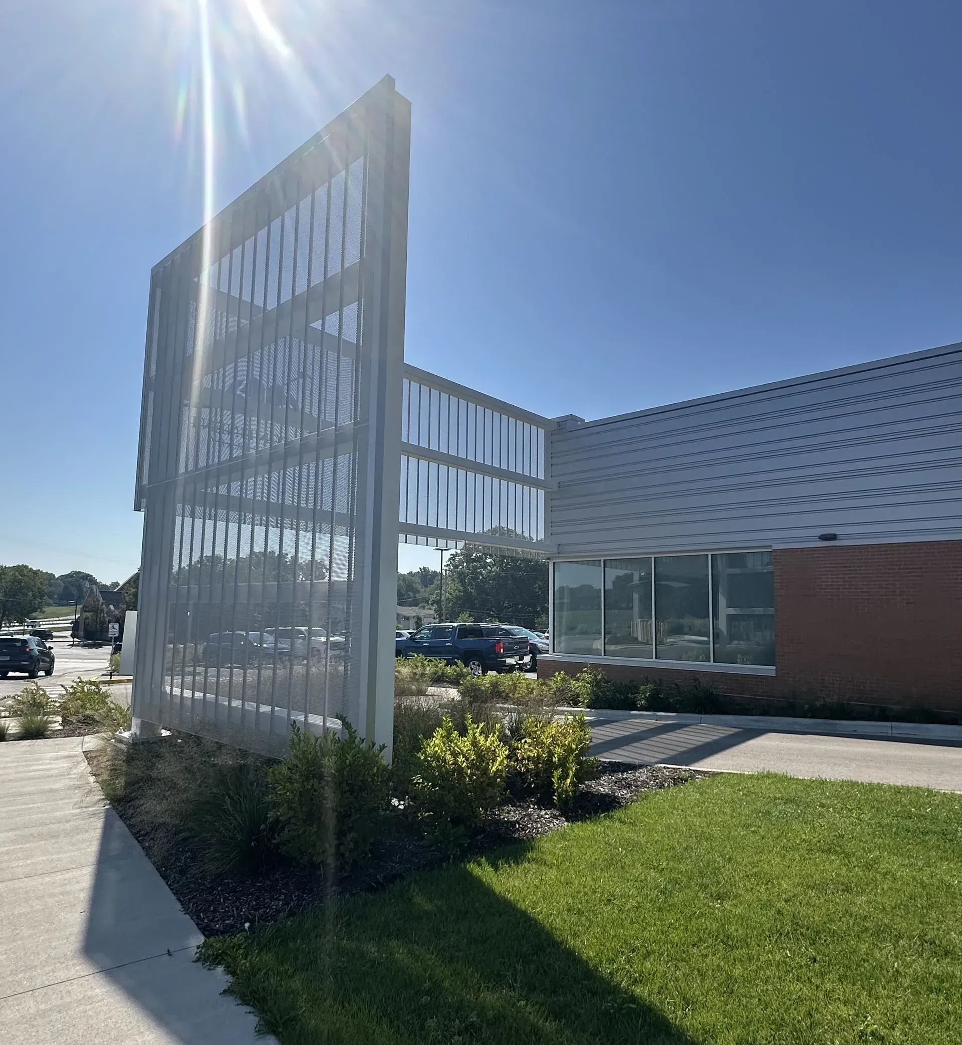 A modern building with a patterned screen, glass walls, and a sloped roof on a sunny day.