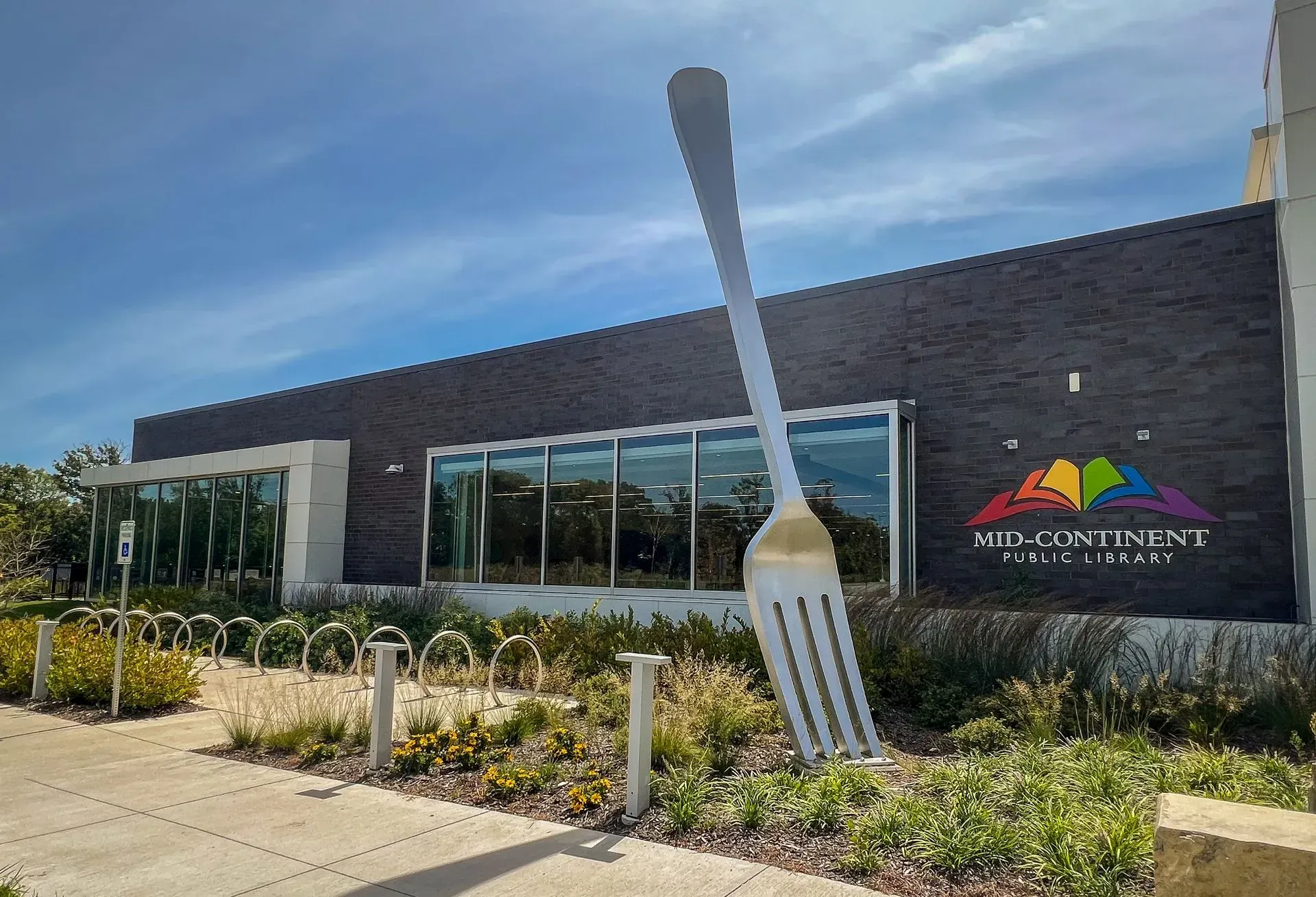 Large fork sculpture in front of the Mid-Continental Library building under a blue sky.
