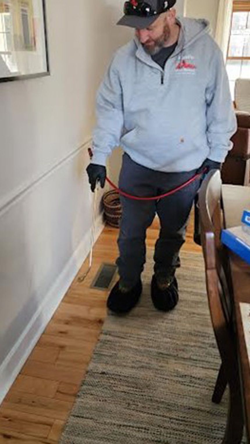 A man is standing in a living room holding a hose.