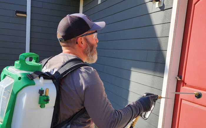 A man is spraying a house with a backpack sprayer.