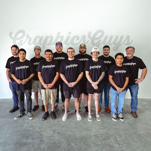 Group of nine people in black T-shirts standing in front of a “Graphite Guys” wall sign.