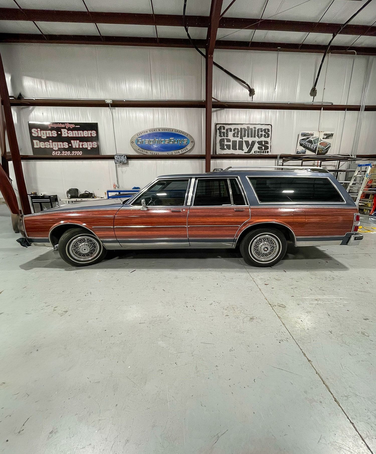 Classic wood-paneled station wagon in a garage showroom, side view with chrome trim and black roof.