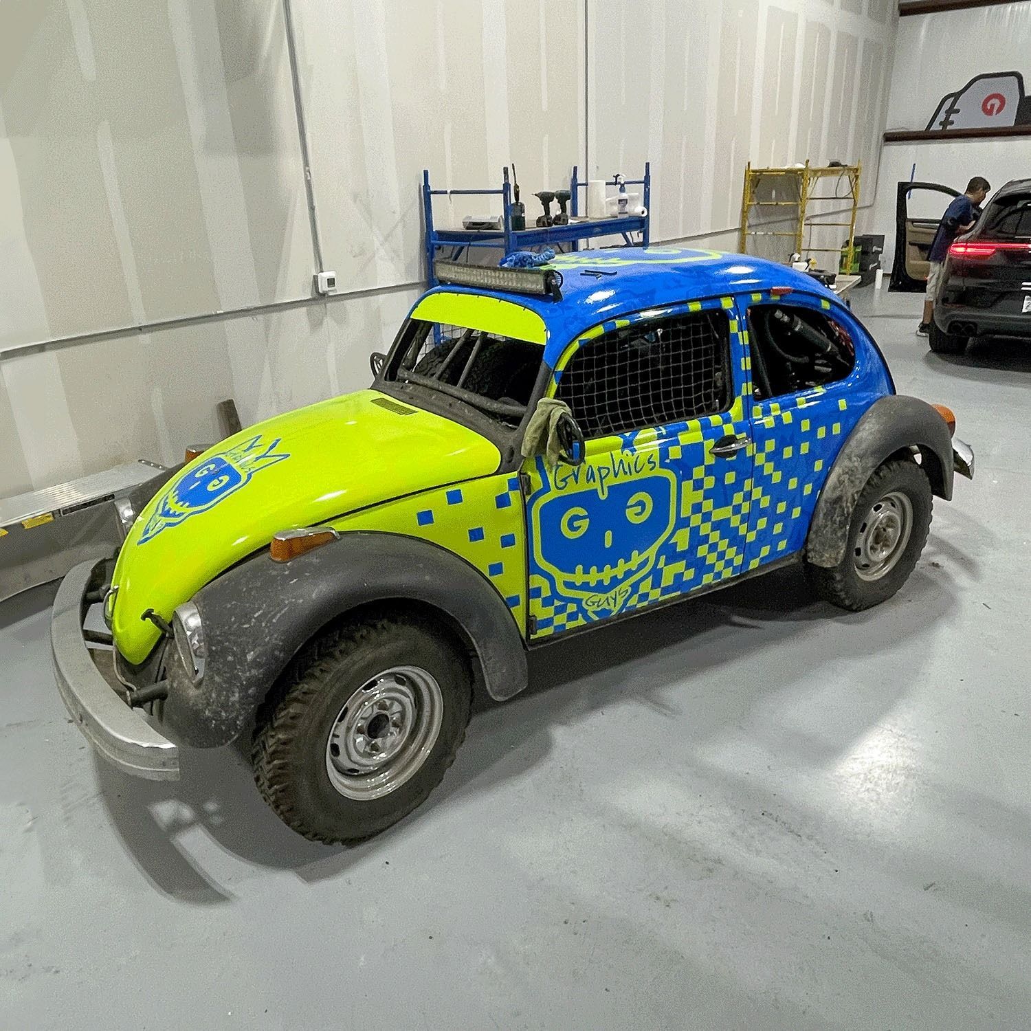 Blue and neon yellow vintage off-road car with patterned graphics, parked indoors on a showroom floor