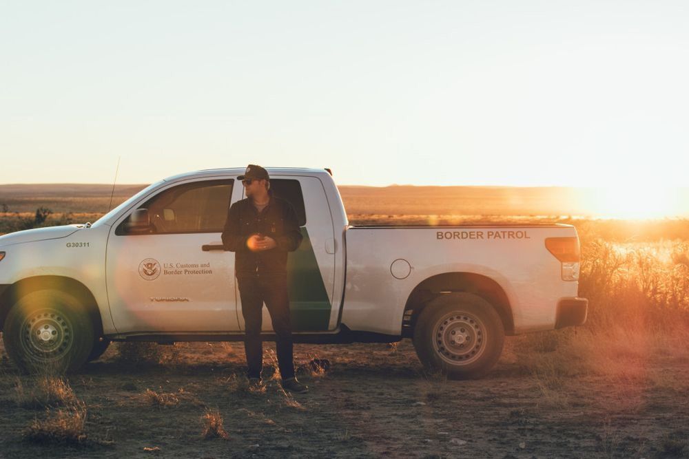 Person standing beside a white utility truck at sunset in a field.