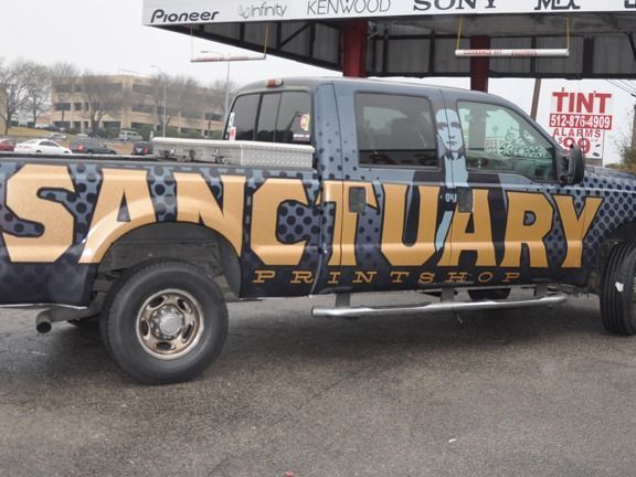 Wrapped truck with large gold “SANCTUARY” lettering parked outdoors at a tint shop