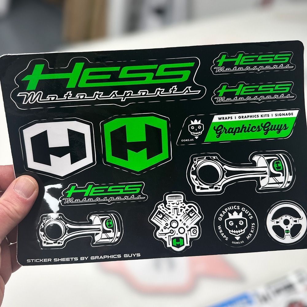 A hand holds a black sheet of neon green and white HESS logo stickers and graphics decals