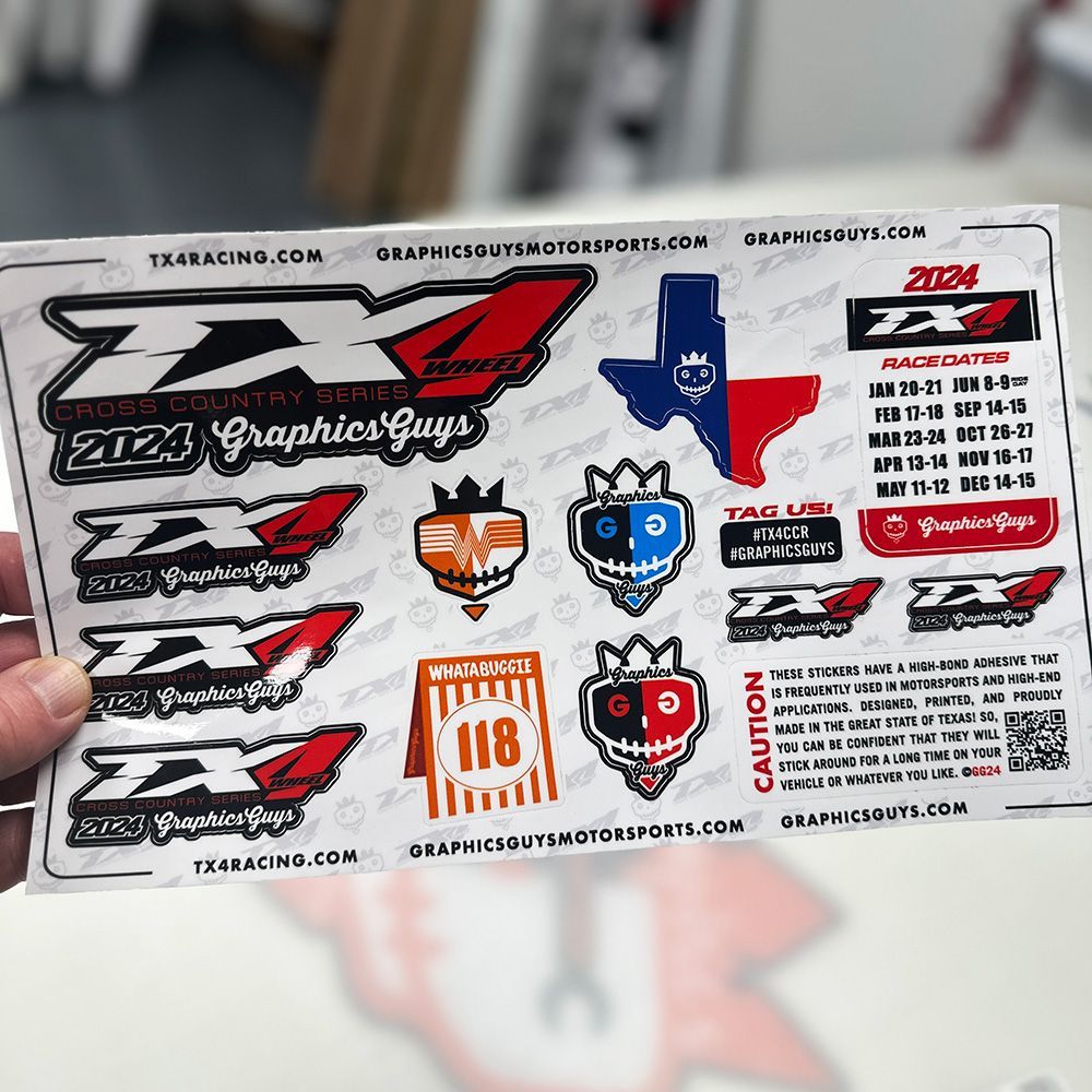 Hand holding a sheet of colorful custom racing decals and logos on a white background