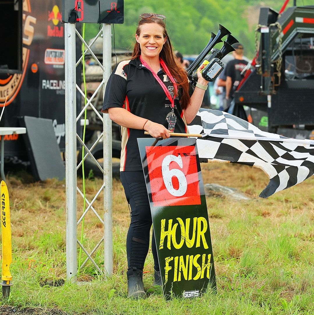 Race official holding a checkered flag at the HCVR finish line, with a red number 6 sign.