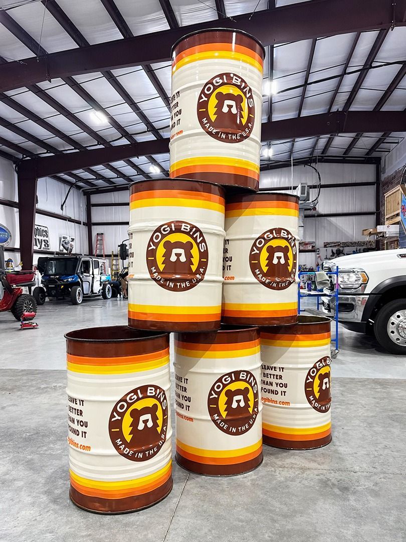 Stacked white industrial drums with orange lids and brown labels in a warehouse
