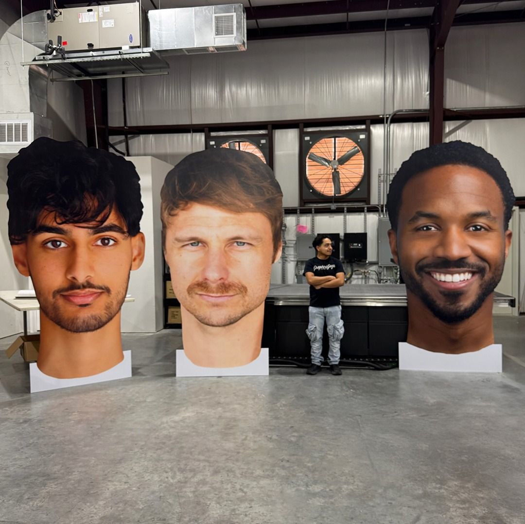 Three large portrait cutouts in an industrial workshop, with a person standing in the background.