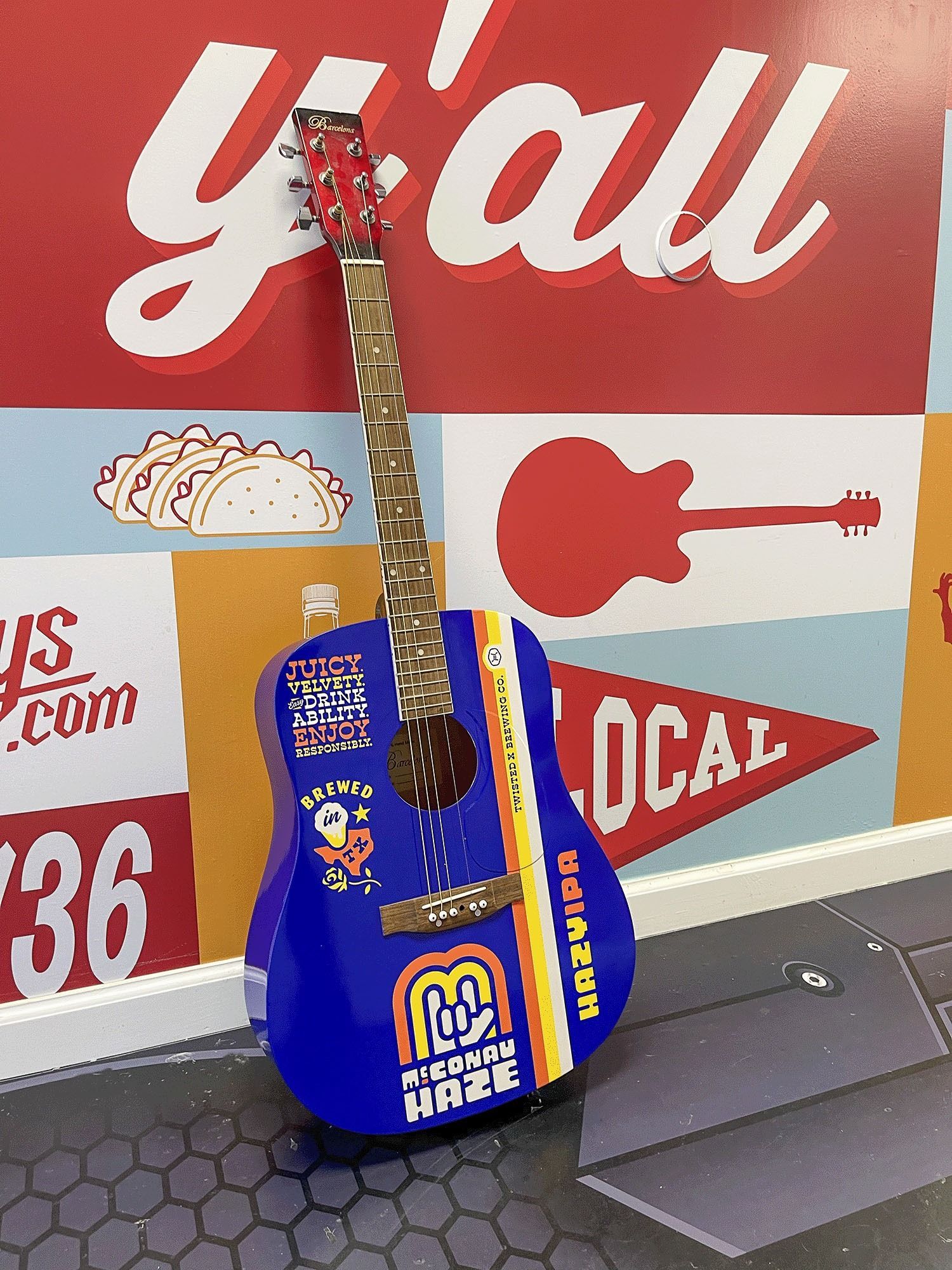 Blue acoustic guitar with orange accents leaning against a red-and-white mural wall.