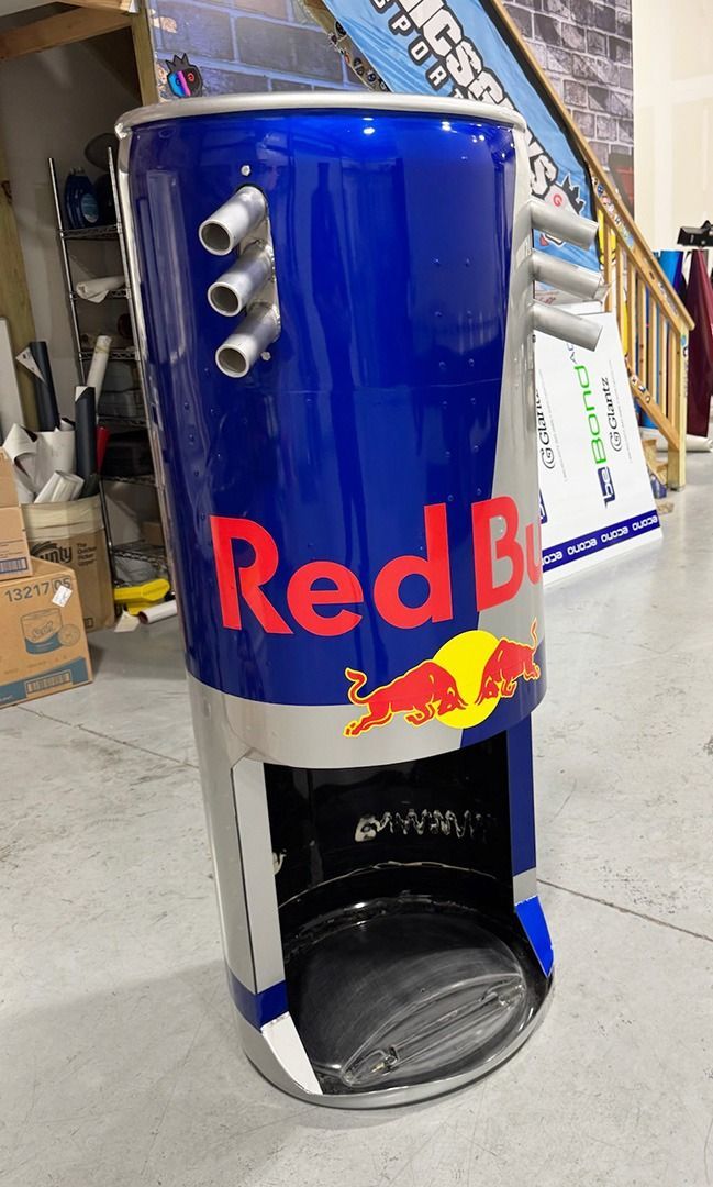 Blue Red Bull-branded cylindrical dispenser with a black opening, standing indoors on a warehouse floor