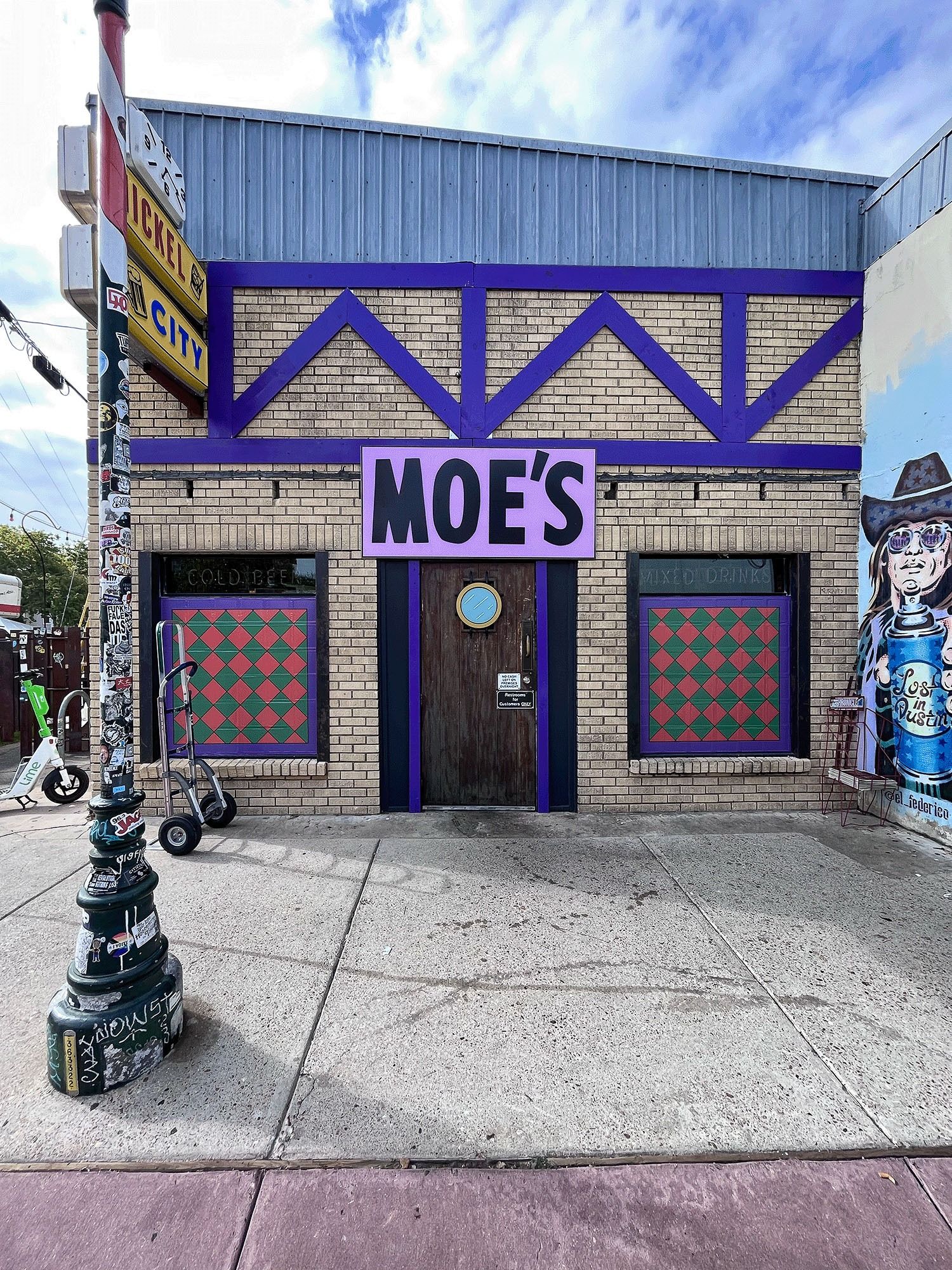 Storefront with a purple-and-blue facade labeled “MOES,” colorful window panels, and a streetlamp outside.