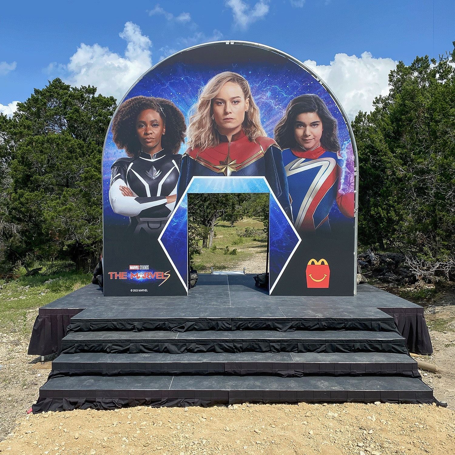 Outdoor movie display with three superhero characters on a large arch backdrop above stone steps