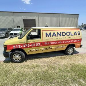 Yellow Mandolas catering van parked on grass outside a warehouse