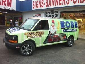 Green KOBO van parked outside a sign shop, with graphics and phone number on the side.