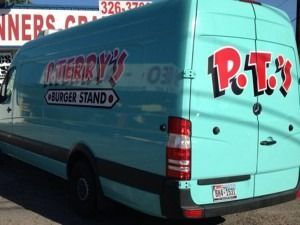 Turquoise P.T.’s Burger Stand delivery van parked outdoors, with restaurant logo on the side.