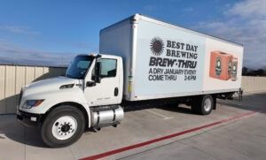 White delivery truck with “Best Day Brewing” ads parked outdoors in a lot.