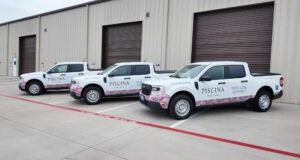 Three white pickup trucks parked outside warehouse garage doors