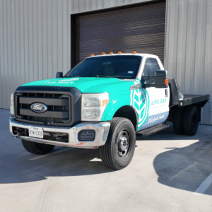 Turquoise and white flatbed tow truck parked outside a metal warehouse.