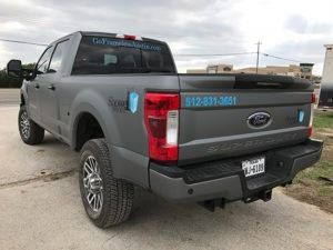 Gray Ford pickup truck with company decals, parked on a concrete lot, rear three-quarter view