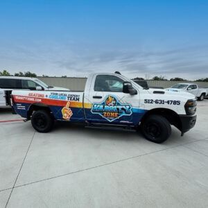 White and black service truck with colorful plumbing graphics parked on a concrete lot under a blue sky