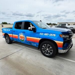 Blue and orange service pickup truck with phone number parked on a concrete lot