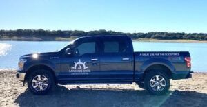 Blue pickup truck with company logo parked on a rocky shore beside a calm lake