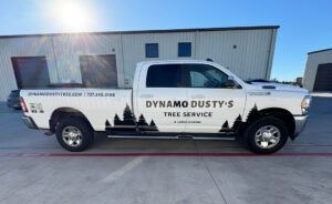 White pickup truck with “Dynamo Dusty’s Tree Service” logo parked beside a warehouse.
