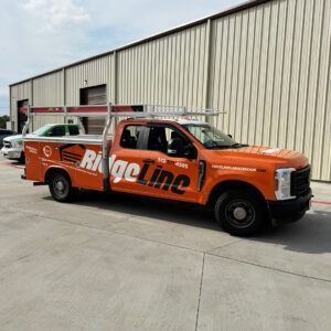 Orange Ring Line service truck parked beside a warehouse, with a ladder on top and a red car behind it